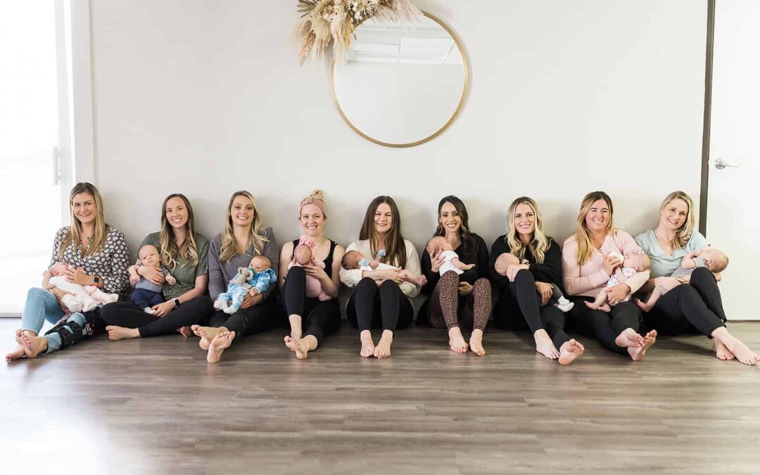 A group of moms sitting against a wall holding their newborns at the New Mom School