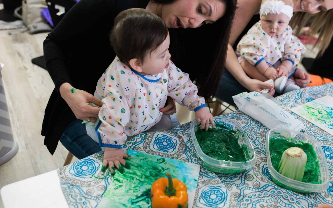 A mom helping her baby paint with green finger paint