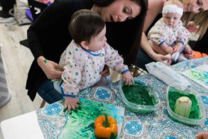 A mom helping her baby paint with green finger paint