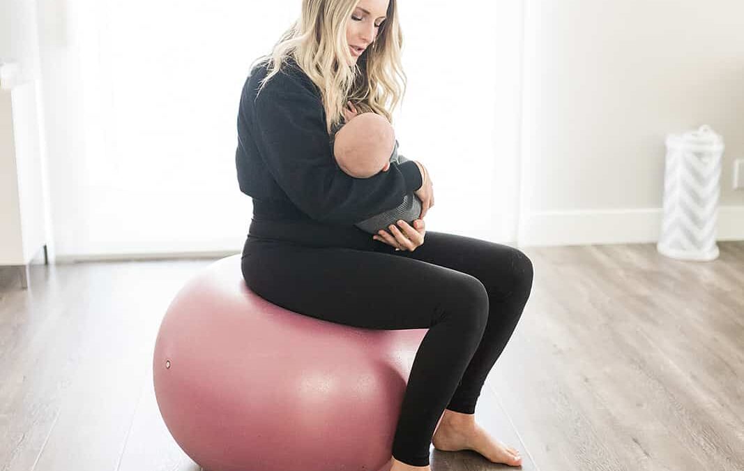 A mother holding her newborn while sitting on a yoga ball
