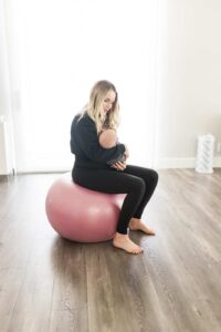 Mom sitting on a yoga ball holding her newborn