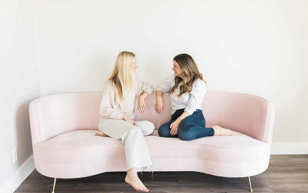 Two Women Sitting on a couch smiling at eachother