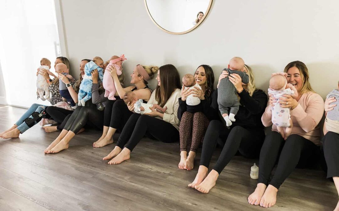 Moms sitting in a line against the wall holding their newborn baby's up