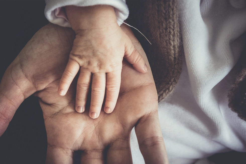 Dad’s hand gently holding a newborn’s hand on Father’s Day.