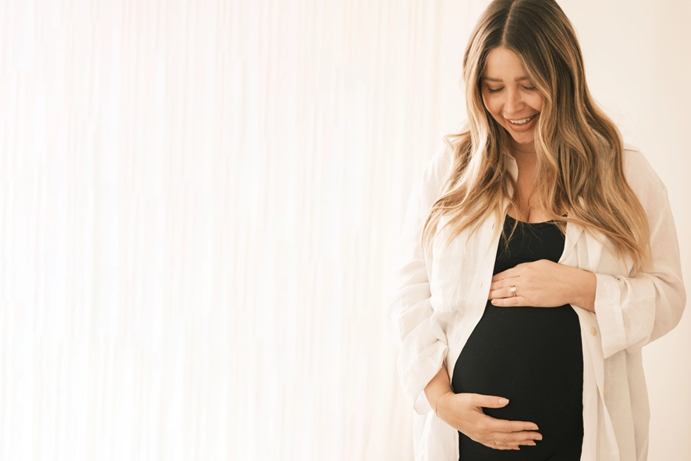 Pregnant woman smiling while reading about New Mom School classes and pre-registration benefits.