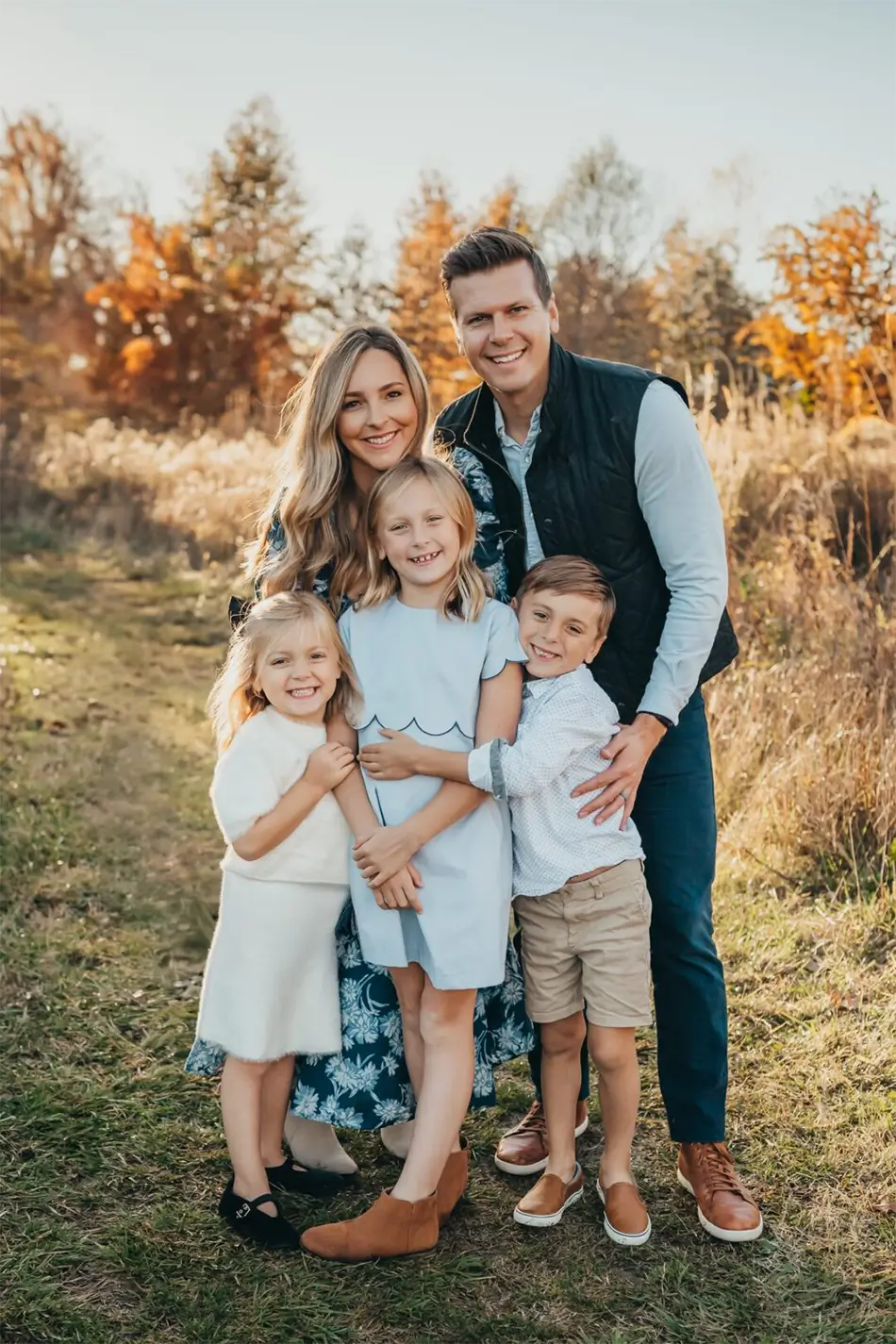 Ali Kochtanek, St. Louis West County. Location Owner of New Mom School, smiling with her husband and three children outdoors in a fall setting.