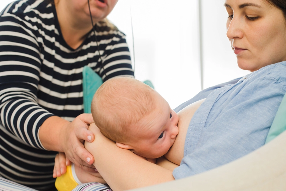 Lactation consultant supporting a mother breastfeeding her newborn baby in Houston Greater Heights, Texas.