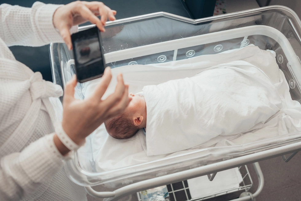 Newborn baby resting in a hospital bassinet while a parent photographs the first moments after birth in Rancho Cucamonga, California.